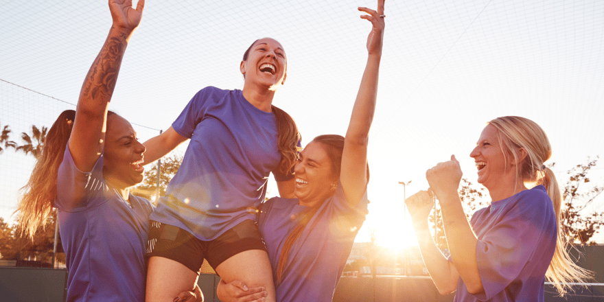Four athletes celebrating together on the field at sunset