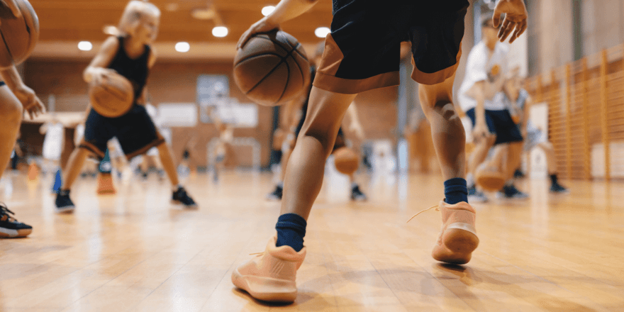Children dribbling basketballs in a gymnasium.
